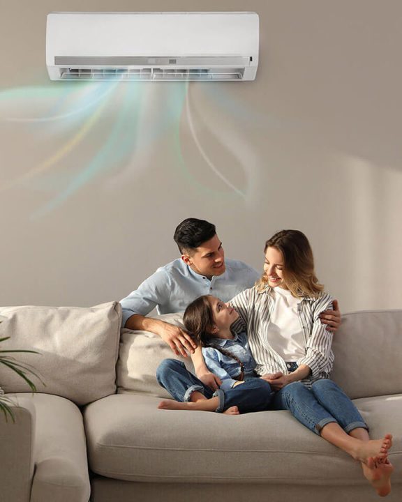 A mom, dad and daughter sit on the couch under a mini-split unit.